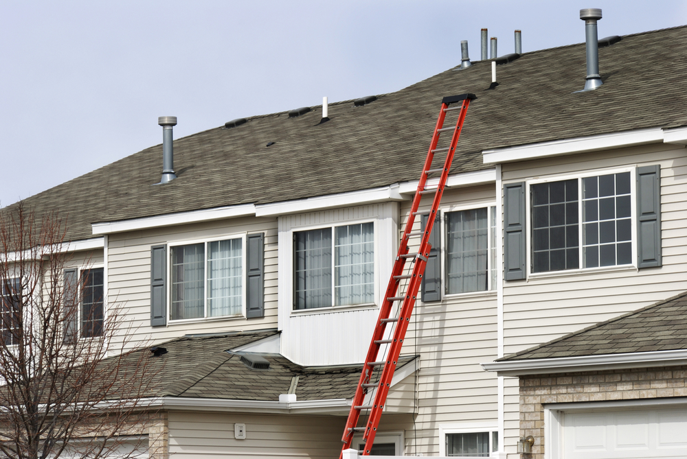 An extension ladder leans against the front of a multifamily housing building in preparation of roof repairs in overland park