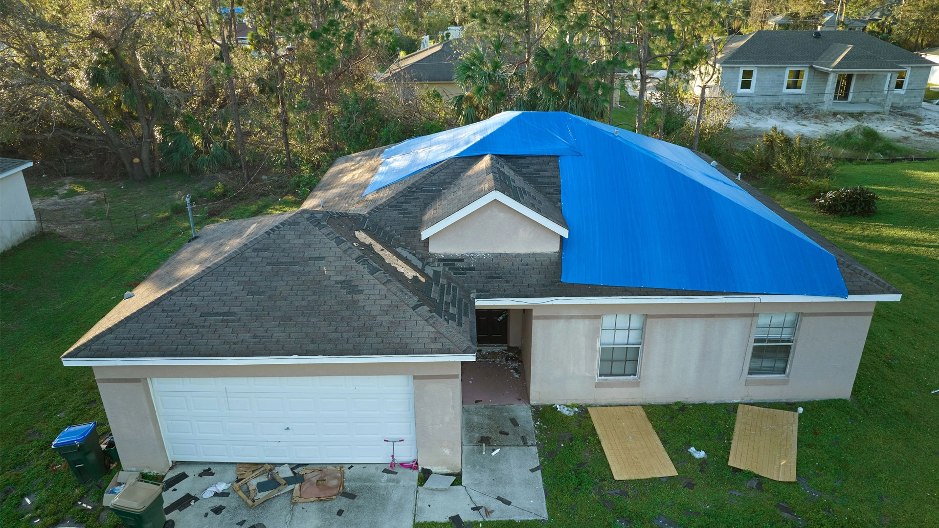 Aerial view of roof damage to house from Hurricane Ian covered in blue tarp for protection from rainwater leaks until asphalt shingles are replaced