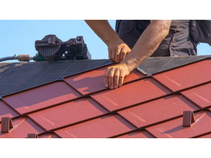 Construction site builder Construction site builder helps lay the roofing atop a modern house. Unrecognizable roofer lays aluminum tiles with the help of a nail gun. Contractor uses power tools during roofing works.
