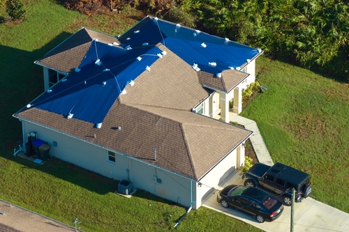 Aerial view of damaged in hurricane Ian house roof covered with blue protective tarp against rain water leaking until replacement of asphalt shingles