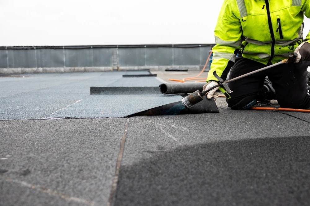 professional roofer applying bitumen roll on flat roof with a gas burner at a modern construction site